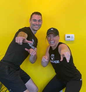 Two people are posing for a picture in front of a yellow wall.