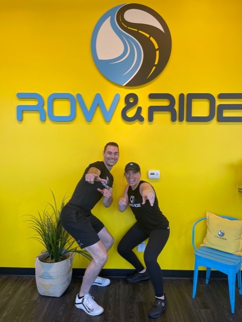 Two people posing in front of a row and ride sign.